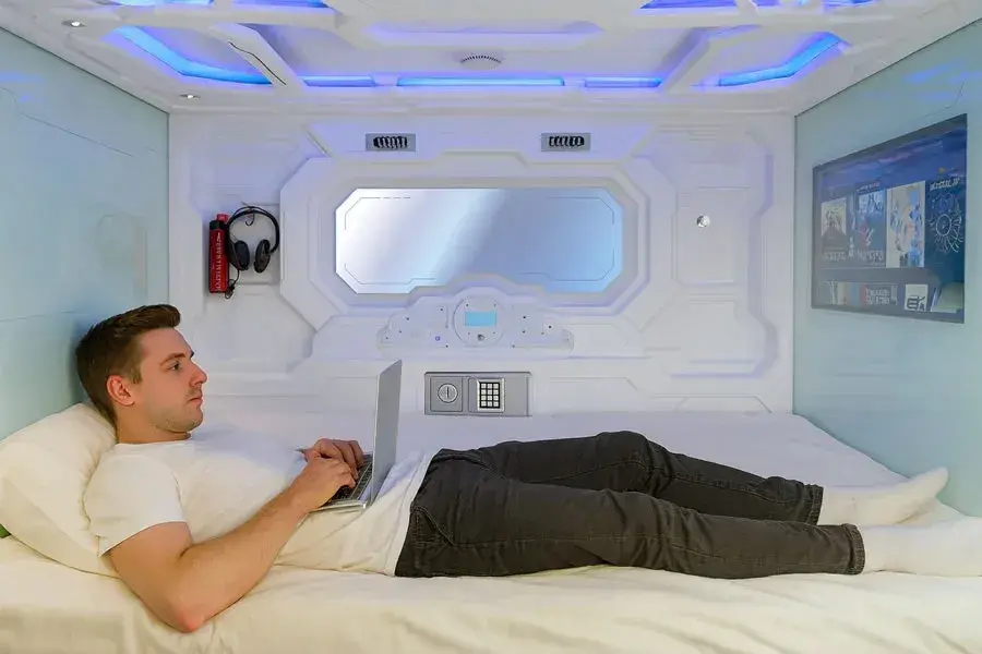 Hombre recostado en c&aacute;psula futurista de Izzzleep en aeropuerto ciudad de Mexico, usando su laptop